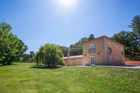 Terracotta-coloured countryside house with a weeping willow tree and expansive green lawn under a sunny sky.
