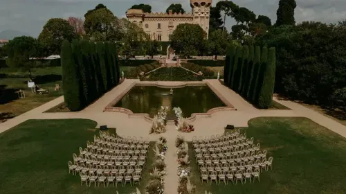 Aerial view of a Barcelona castle venue with manicured hedge gardens, reflecting pool and ceremony seating on the lawn, hosts up to 800 guests