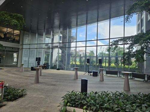 Glass-walled atrium event space with tall ceilings, high cocktail tables, tropical planting and a mezzanine level above.
