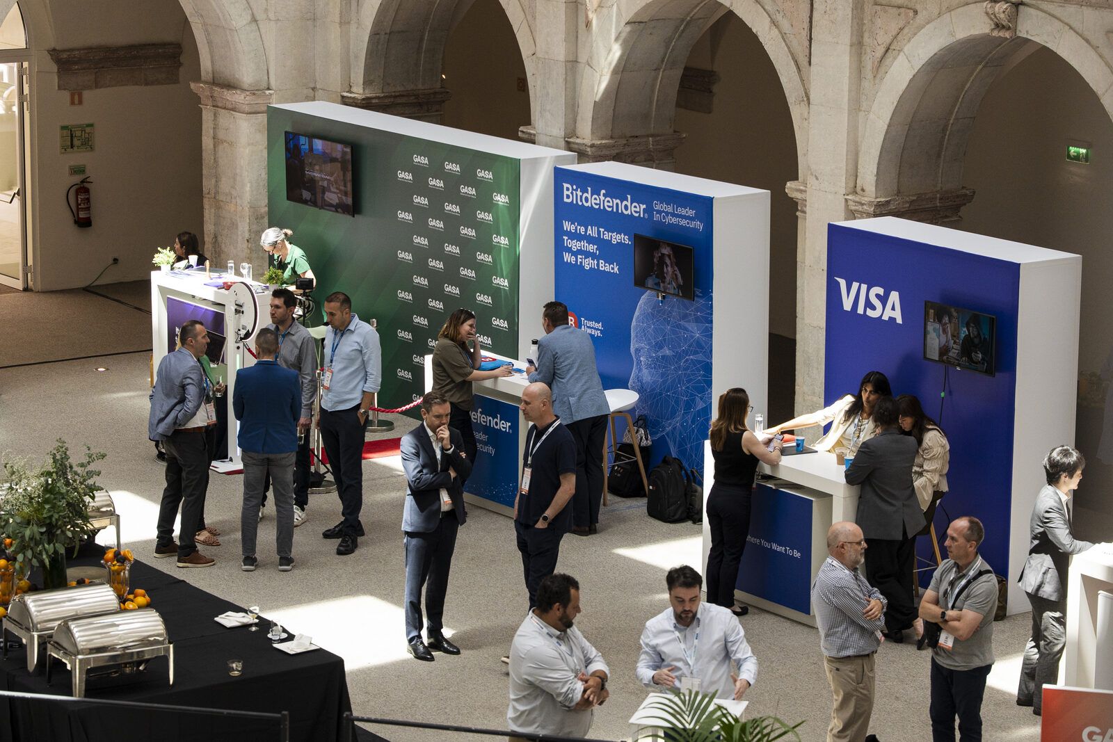 Attendees at sponsor booths including Bitdefender and Visa in the expo area at Convento do Beato
