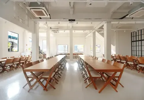 Bright minimalist event space in Singapore with white walls, exposed ceiling ductwork and long wooden banquet tables, hosts up to 300 guests