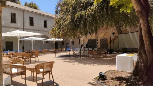 Renaissance cloister courtyard in Milan with white parasol seating areas, rattan chairs and mature shade trees, seats up to 250 guests