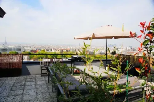 Rooftop terrace with lounge seating, umbrella and plants overlooking the Paris skyline and Eiffel Tower