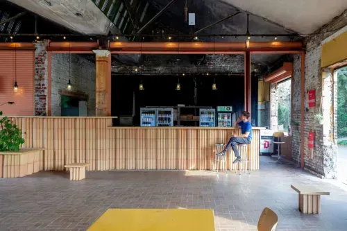 Industrial-style bar interior with exposed brick, string lights and wooden counter, garden visible through an open doorway