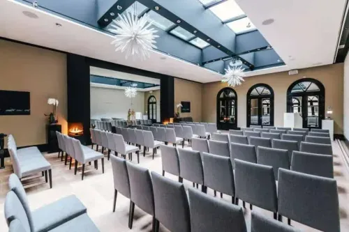 Skylit event hall in Amsterdam with Art Deco starburst chandeliers, theatre seating and arched windows, hosts up to 150 guests