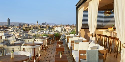 10th-floor rooftop terrace in Barcelona with rattan lounge seating, cabana curtains and panoramic city skyline view, hosts up to 95 guests