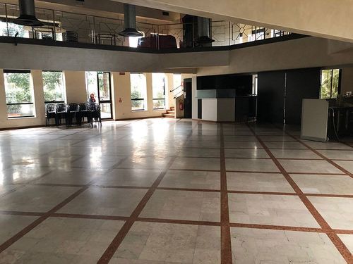 Large empty banquet hall in a historic Milan farmhouse with marble flooring, terracotta inlay lines, tall windows and a mezzanine level above.