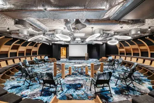 Atlantis-themed auditorium in Brussels with an ocean-motif floor, curved wooden tiered seating and metallic ceiling ducting, set up for a conference.