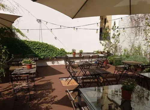 Secret garden terrace in Milan with wrought iron tables and chairs, string lights, large umbrellas, potted plants and climbing ivy along the walls.