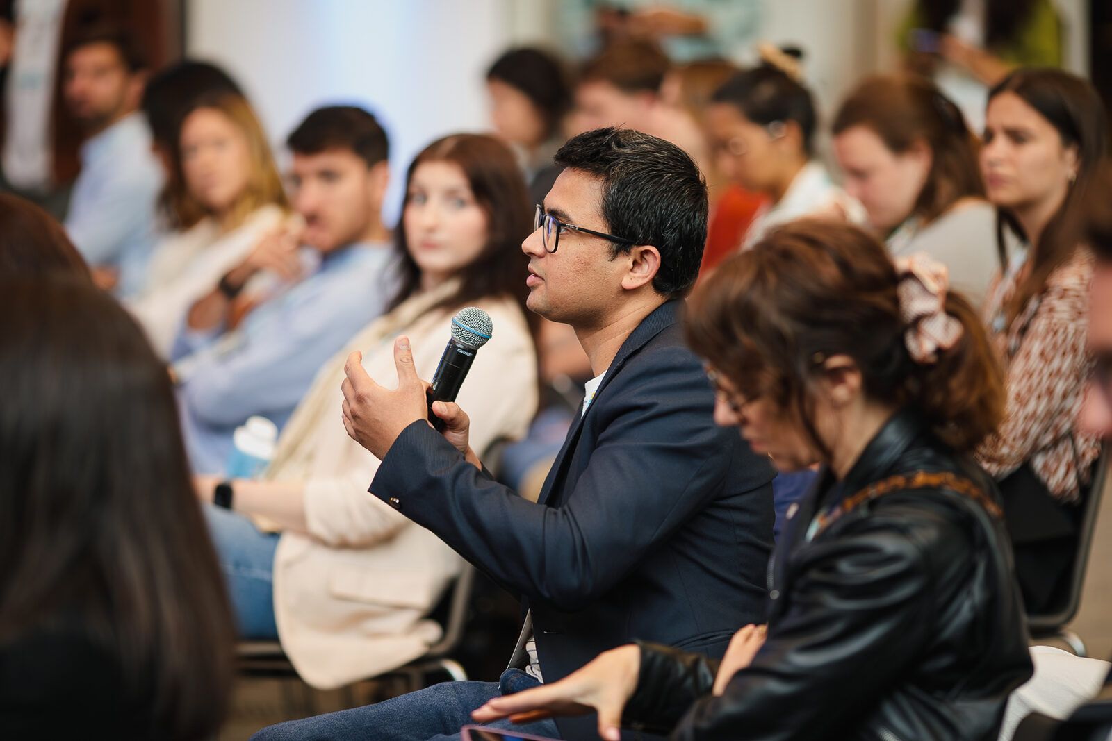 Attendee holding a microphone asking a question during a conference session, audience seated around him