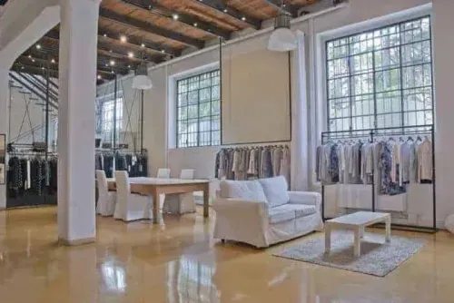 Converted early-1900s rice mill in Milan with exposed timber beam ceiling, clothing rails and white lounge seating, fashion showroom setup