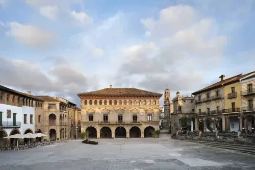 Monumental stone plaza framed by historic Spanish architecture and a clock tower, wide open cobbled square