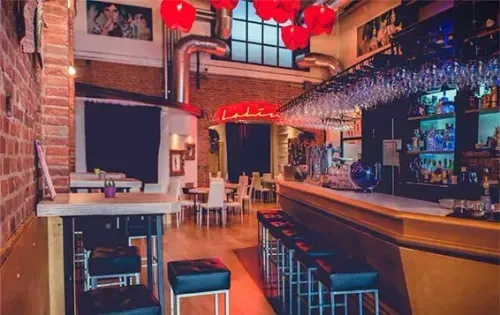 Industrial-style bar venue in Madrid with exposed brick walls, red neon lighting and hanging glassware over the bar, hosts up to 200 guests