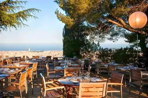 Hilltop terrace dining at a Barcelona observatory with wooden tables set among pine trees and panoramic city and sea views, hosts up to 350 guests