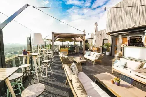 Rooftop terrace in Amsterdam with lounge sofas, bar area and reed screen walls overlooking the city skyline, cocktail party setting 85 metres up