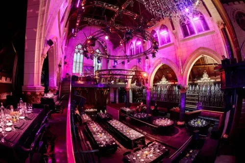 Converted Anglican church venue in Brussels with Gothic arches lit in pink and purple, rigged lighting truss and cabaret table seating, hosts up to 650 guests